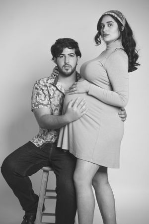 Black and white maternity photo of couple in casual attire posing together.