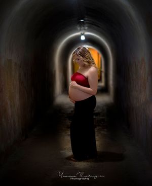 A dramatic maternity silhouette photograph taken in a dark tunnel with warm lighting in the background.