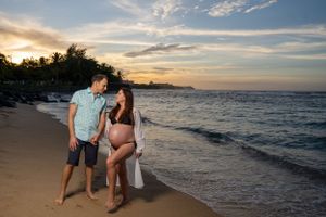 Couple shares intimate moment during sunset beach maternity photoshoot.