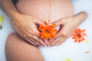 Close-up of pregnant belly with orange flower in milk bath setting.