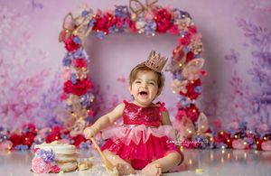 Festive pink and red floral birthday setup with cake and decorations against dreamy purple background.