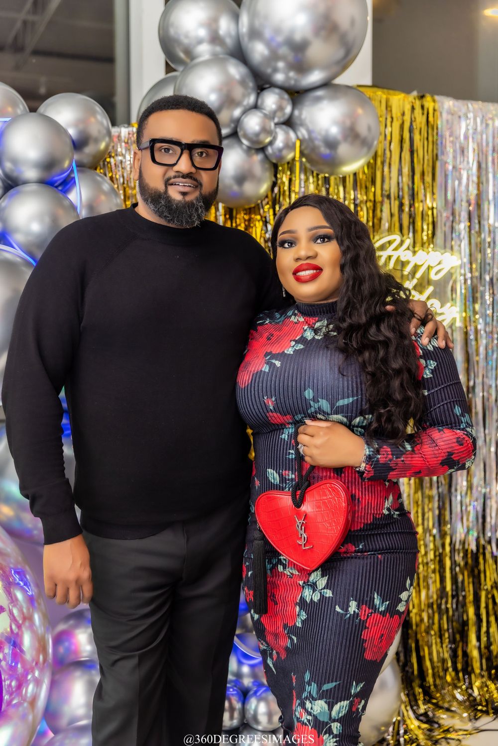Couple posing together at elegant party with silver and gold balloon backdrop and metallic fringe curtains.