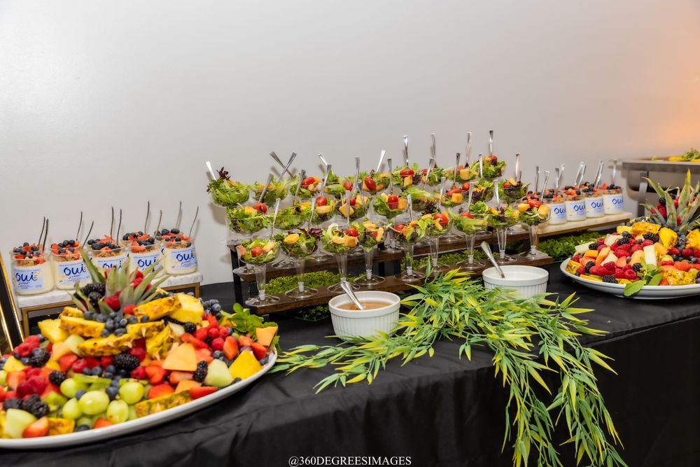 Elegant buffet table with colorful fruit displays, salad cups in glasses, and fresh vegetable arrangements.
