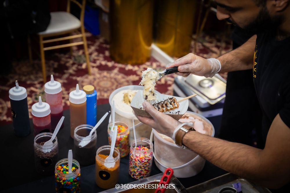 Caterer preparing gourmet ice cream sundaes with toppings and colorful candy at a dessert station.