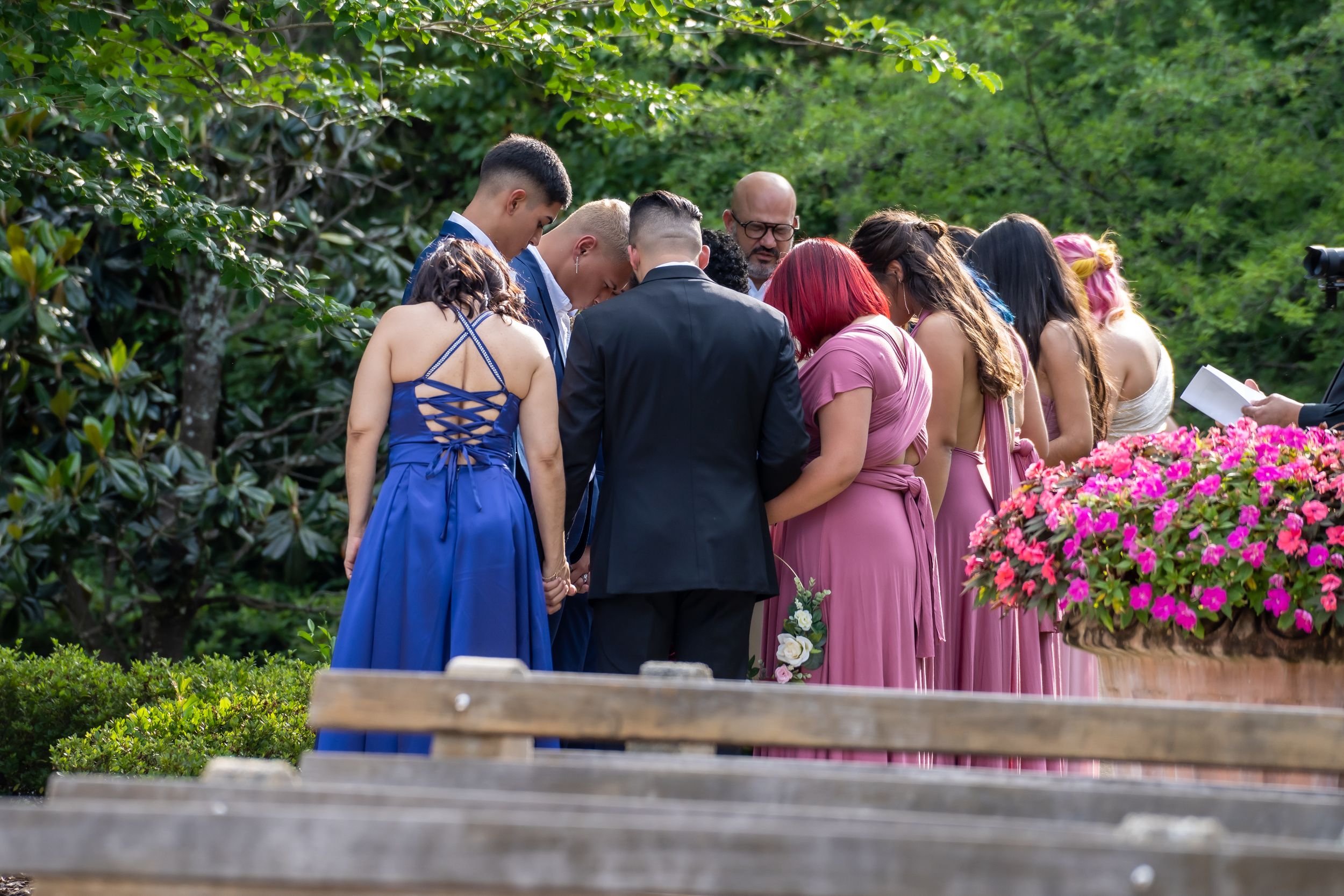 Wedding party members in colorful dresses stand together during an outdoor ceremony.