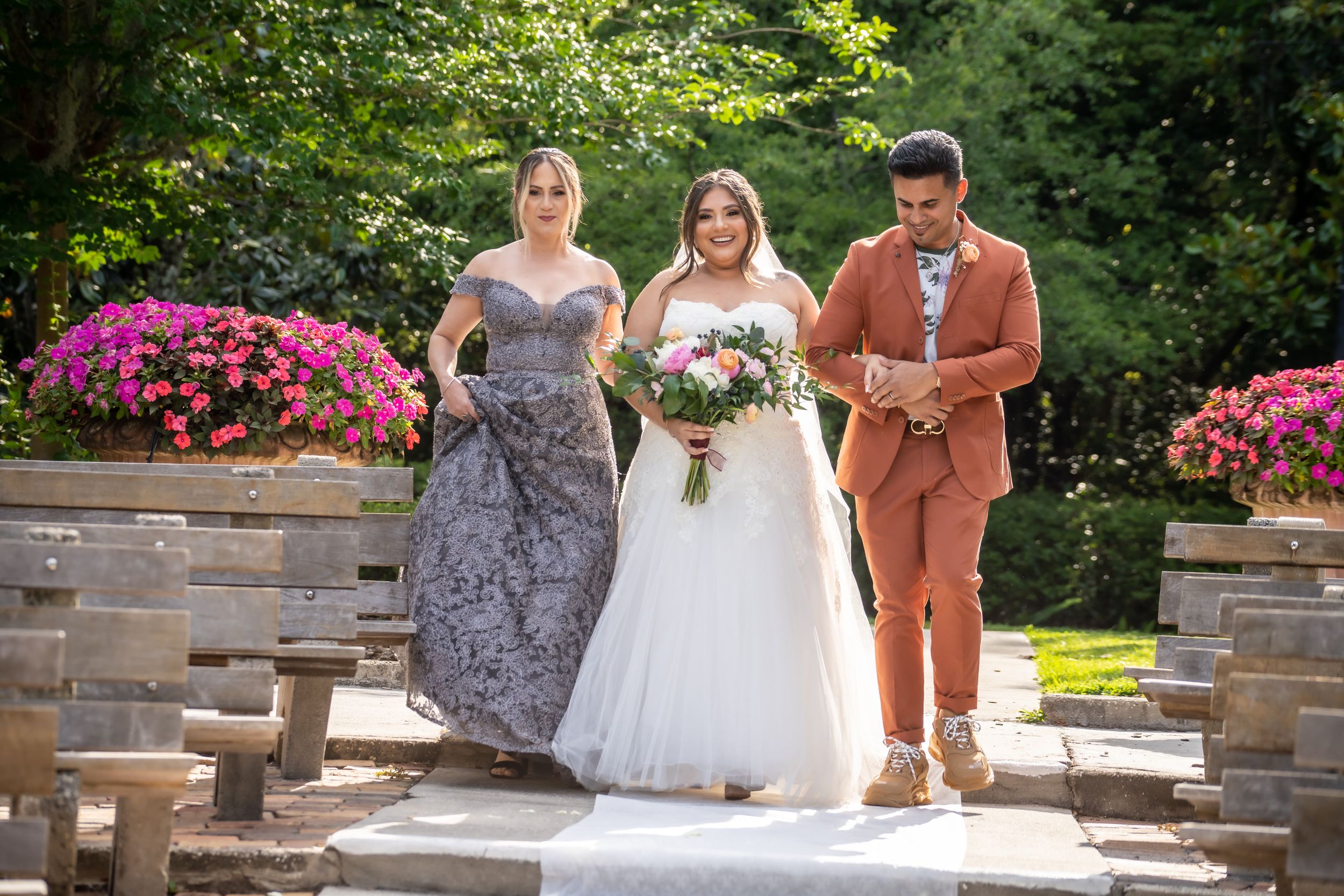 A wedding party walks down stone steps surrounded by blooming azalea bushes in a garden setting.