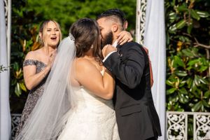 A wedding ceremony moment captured under an ornate white gazebo in a garden setting.