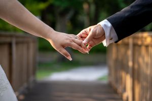 Close-up of newlyweds holding hands, showing wedding rings and formal attire.