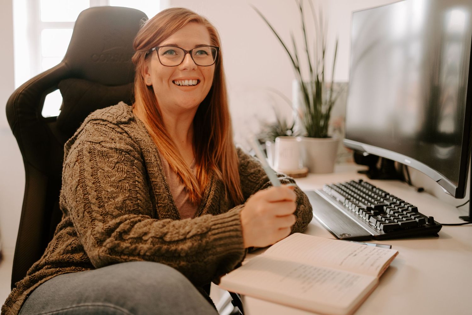 Professional working at a desk with laptop, coffee, and plants in a modern office setting.