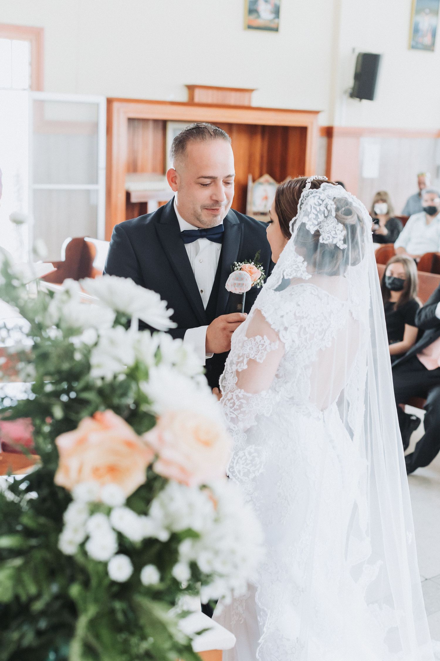 A wedding ceremony in progress with white floral decorations in an indoor venue.