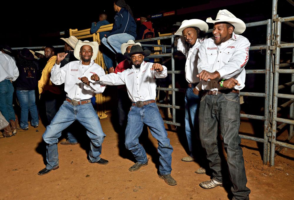 Cowboys dancing and having fun at a rodeo event while others watch from behind metal gates.