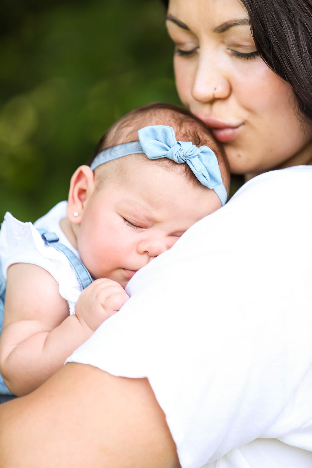 Baby wearing blue headband sleeps peacefully on parent's shoulder.