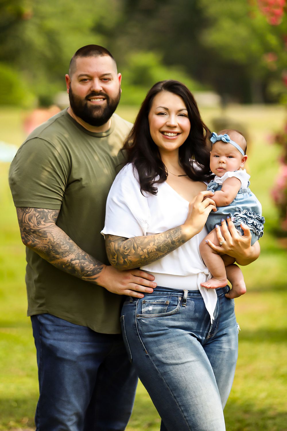 Family of three poses outdoors in casual attire against natural background.