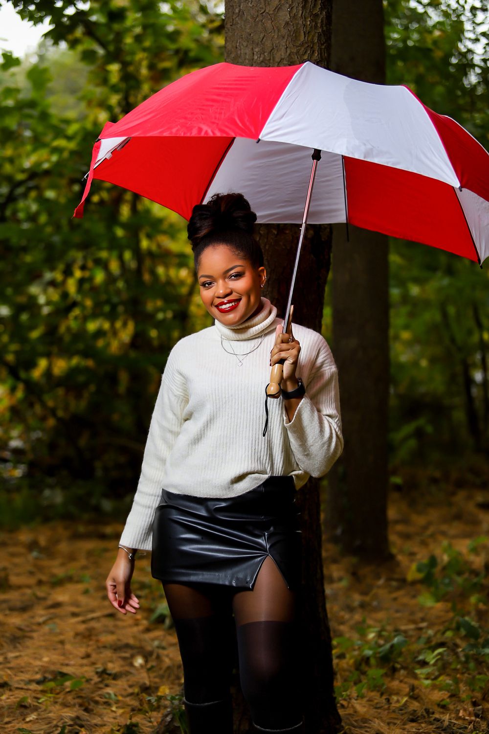 Someone walking with a red and white umbrella through a wooded path wearing a white sweater.