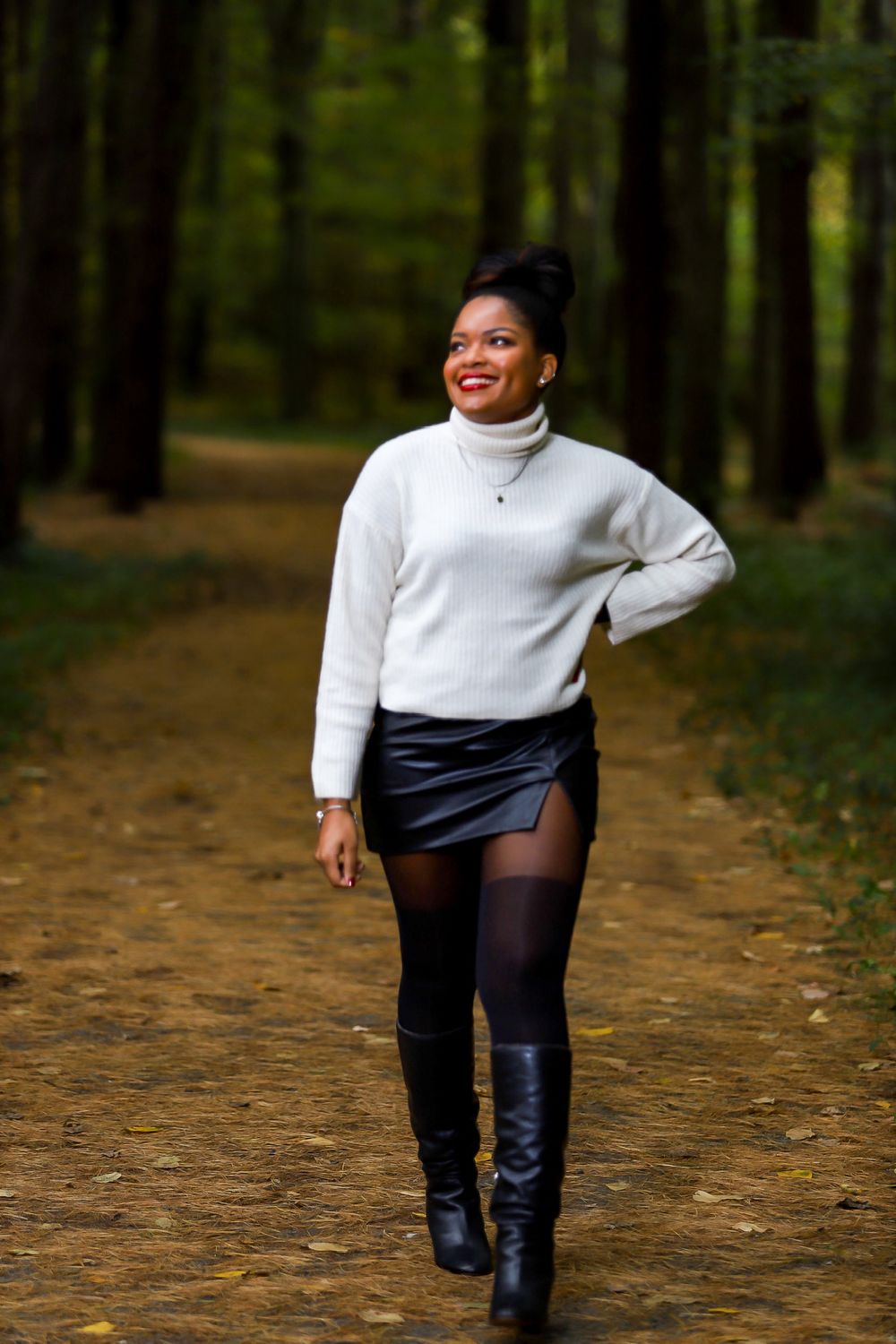 A person in a white sweater and black boots walks through a forest path during autumn.