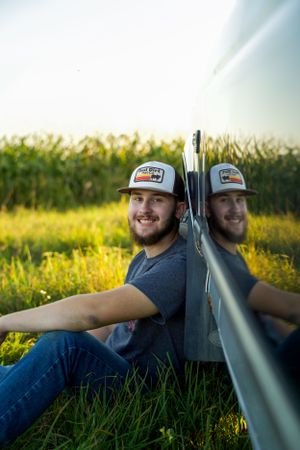 Two hunters with rifles sit back-to-back in grassy field at sunset.