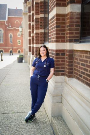 Medical professional in navy scrubs leans against brick building exterior.