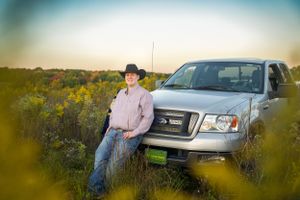 Rustic portrait beside pickup truck in wildflower field at dusk.