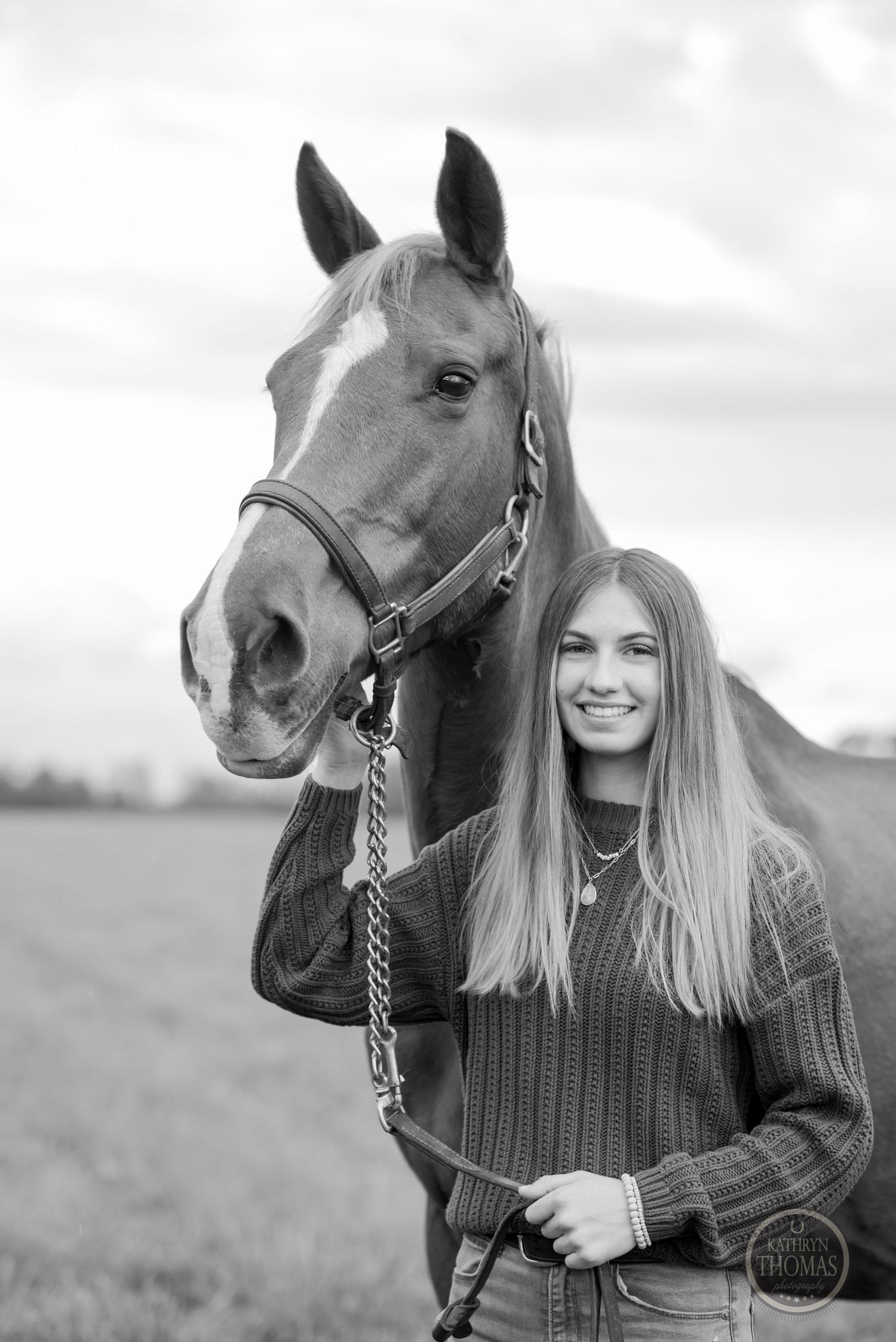 A black and white portrait of a horse and companion in a sweater against an overcast sky.