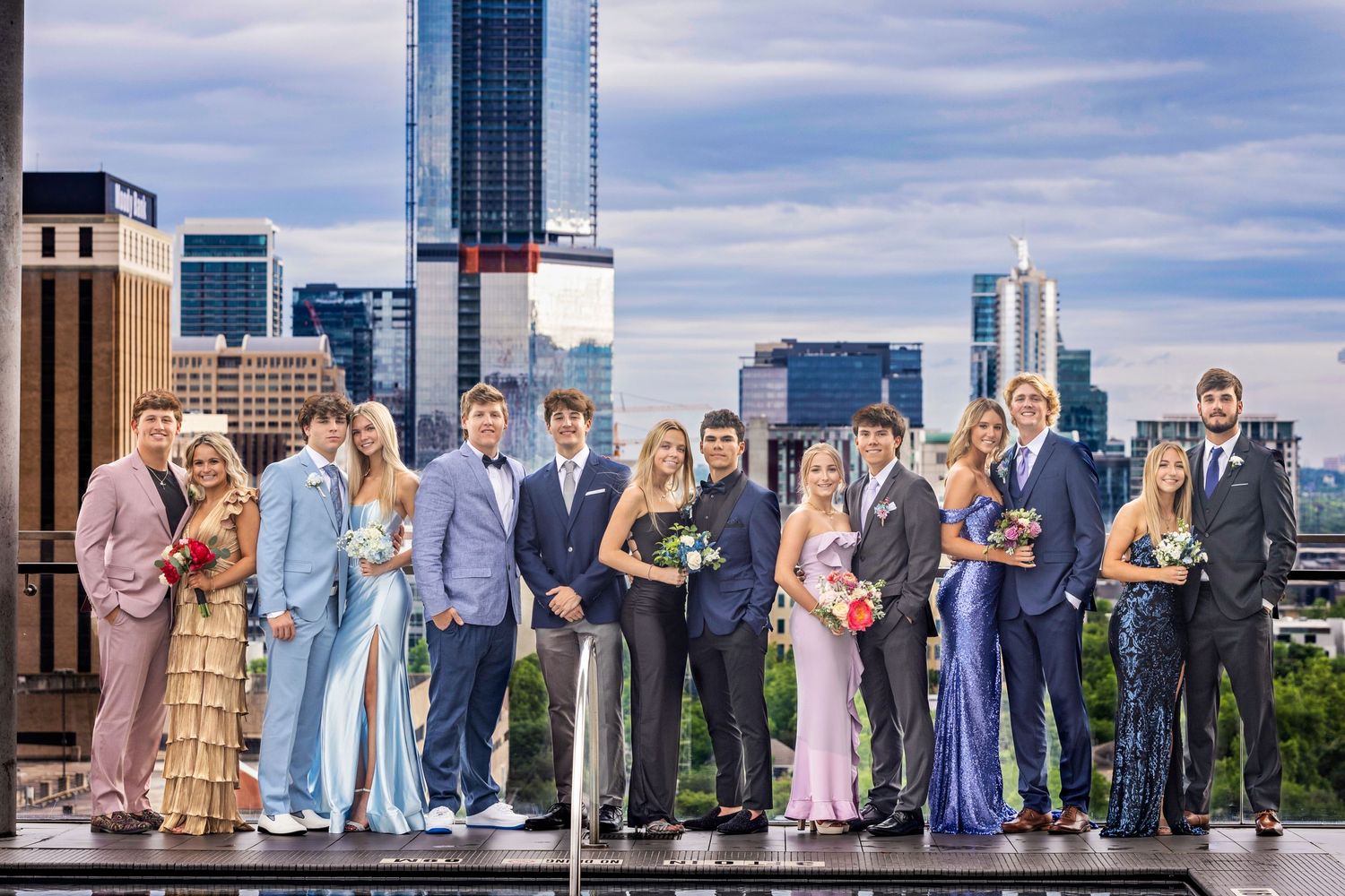 A formal group poses on a rooftop with city skyline views in the background.