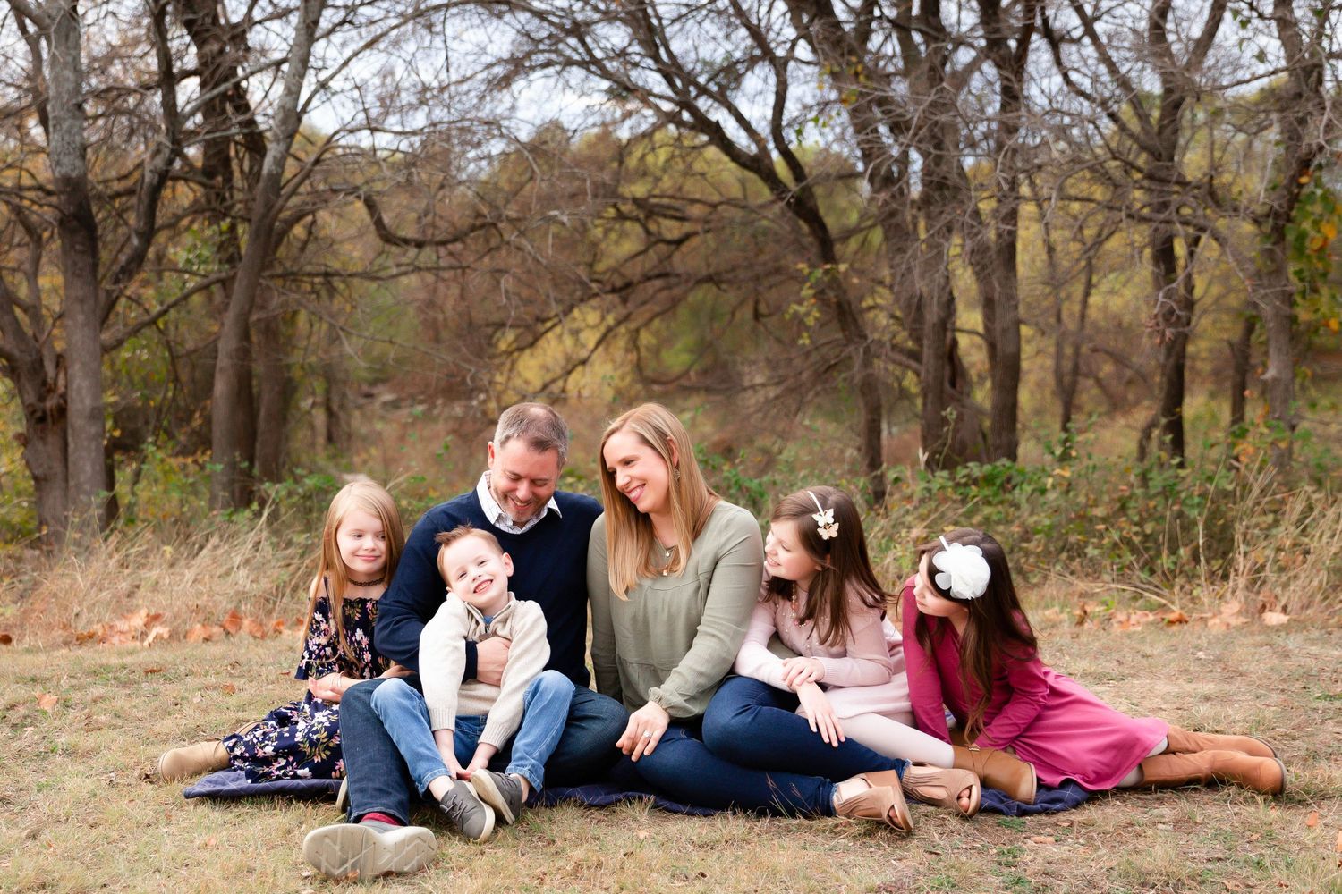Family group relaxing together outdoors on fallen autumn leaves.