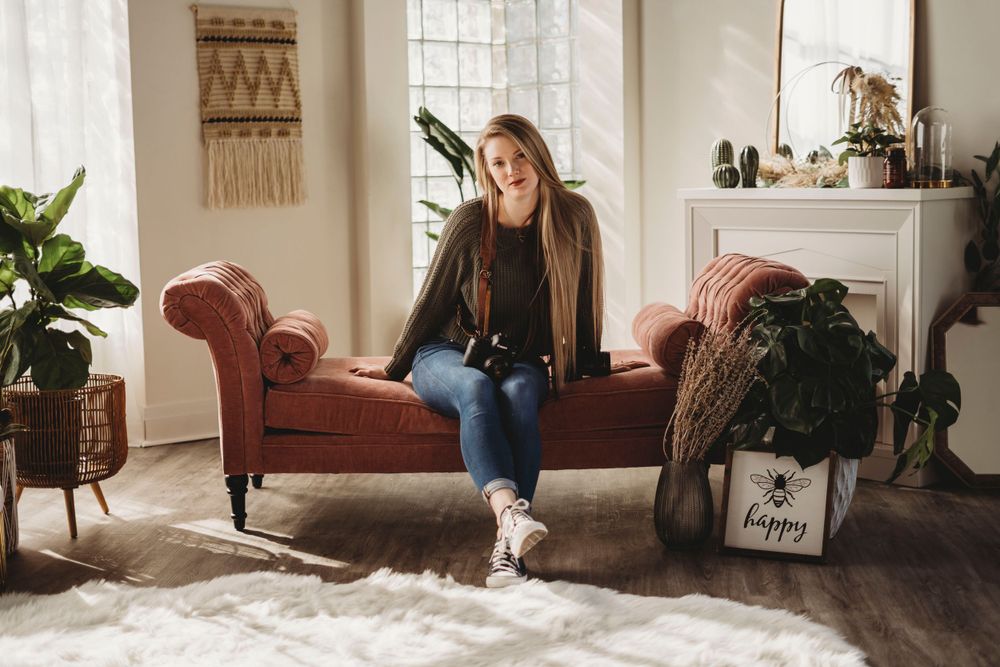 A relaxed lifestyle portrait on a vintage red velvet couch in a bright, plant-filled room.