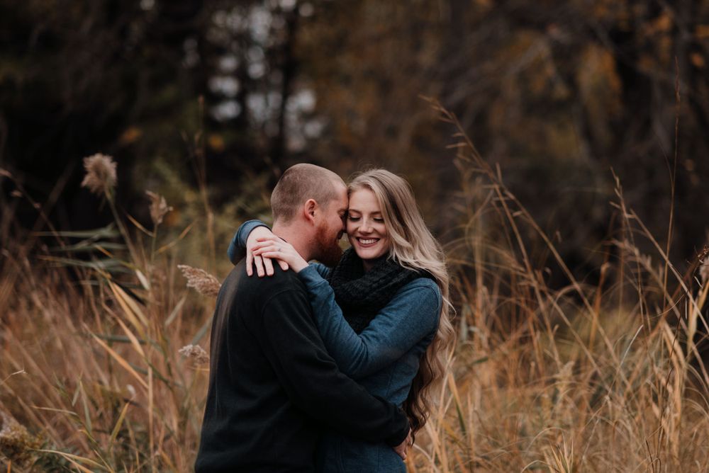 Two people embracing outdoors in a field of tall brown grass on an autumn day.