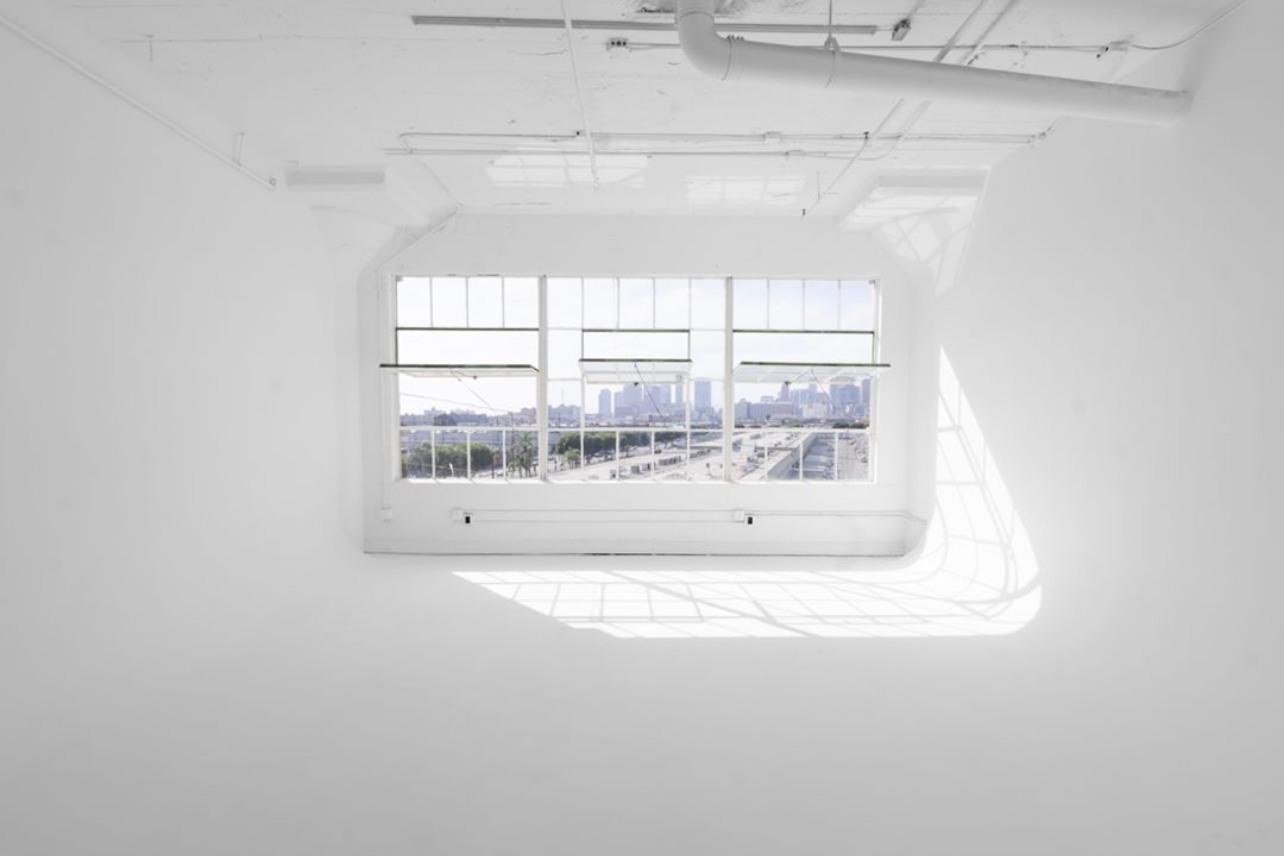 Bright minimalist white room with row of windows offering view of city skyline.