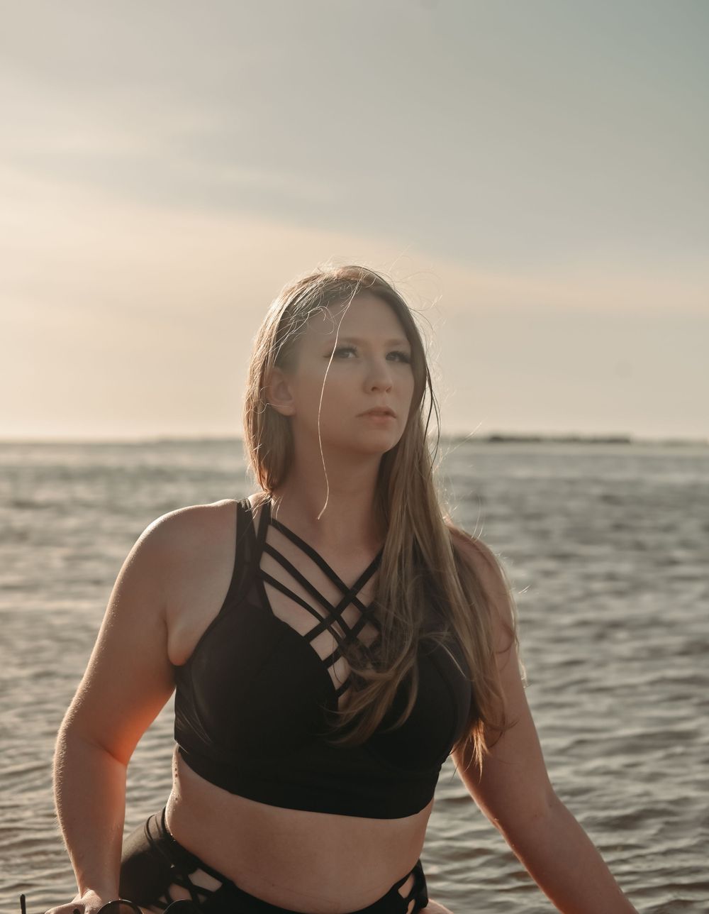 Portrait in strappy black swimwear against ocean horizon at sunset.