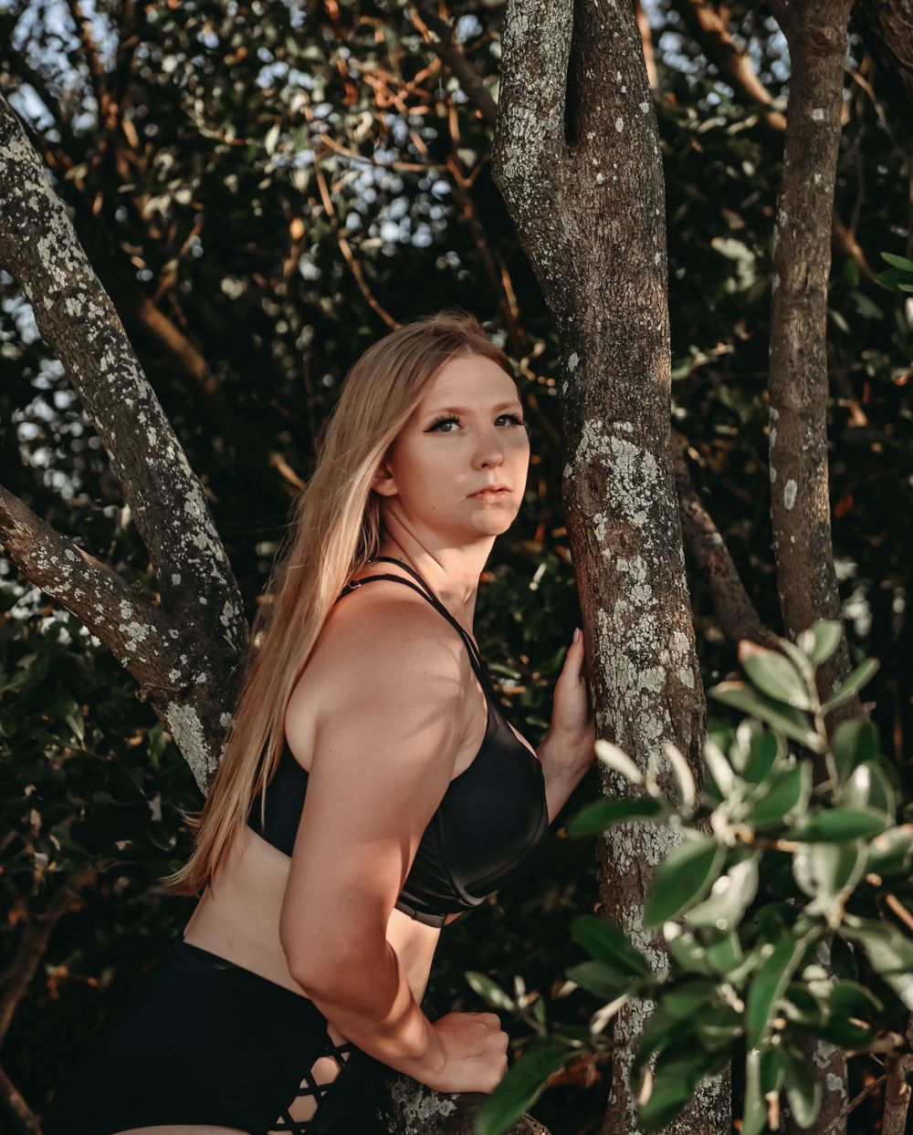 Athletic silhouette posed among tree branches in natural outdoor setting.
