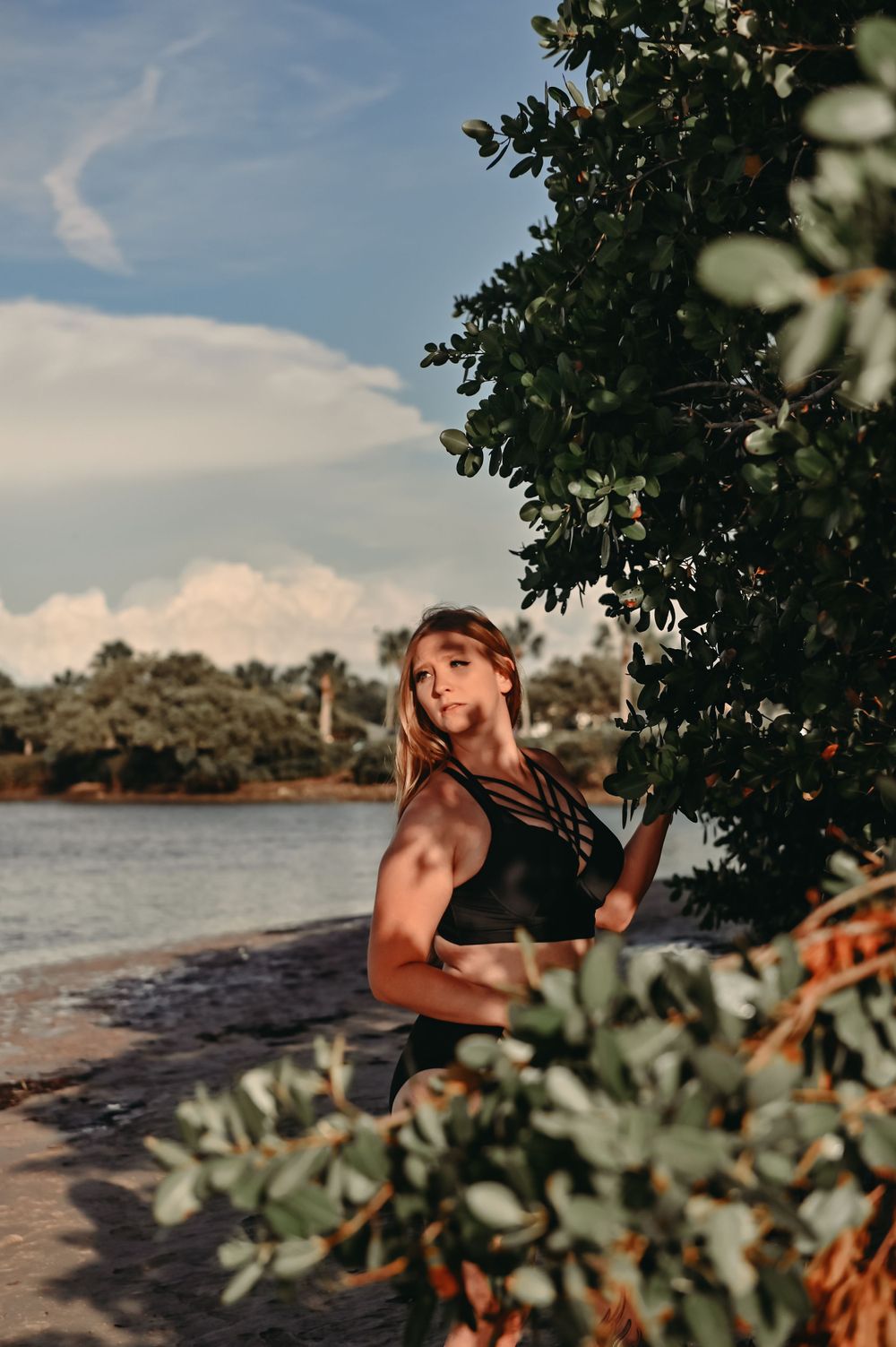 Fitness photoshoot by the water with lush greenery framing the scene at sunset.