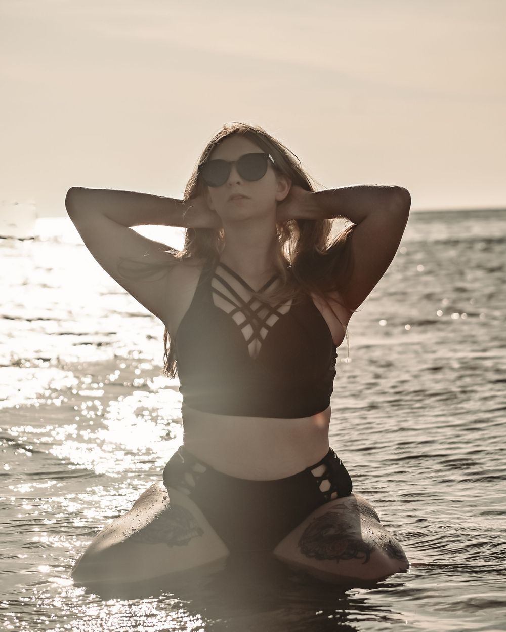 Silhouette in black swimwear posing in ocean water during golden hour.