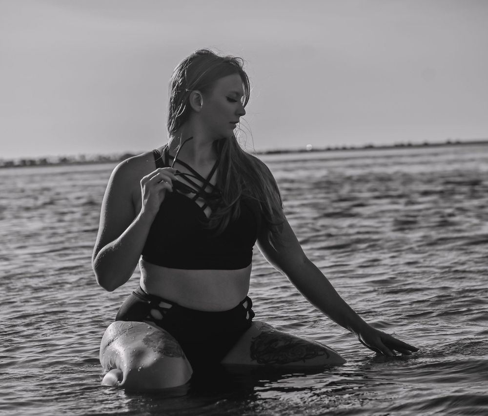 Monochrome photo of figure in strappy swimwear posed in ocean water.
