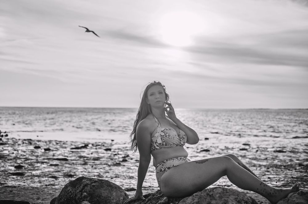 Black and white beach portrait with seabird flying overhead against ocean backdrop.