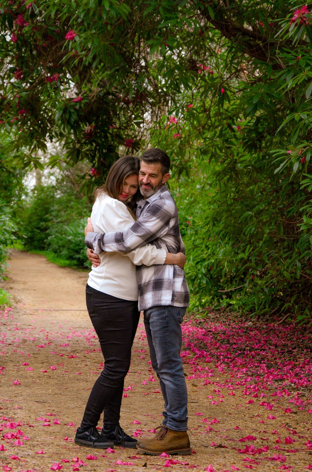 Couple embracing on pathway with pink flower petals scattered on ground.