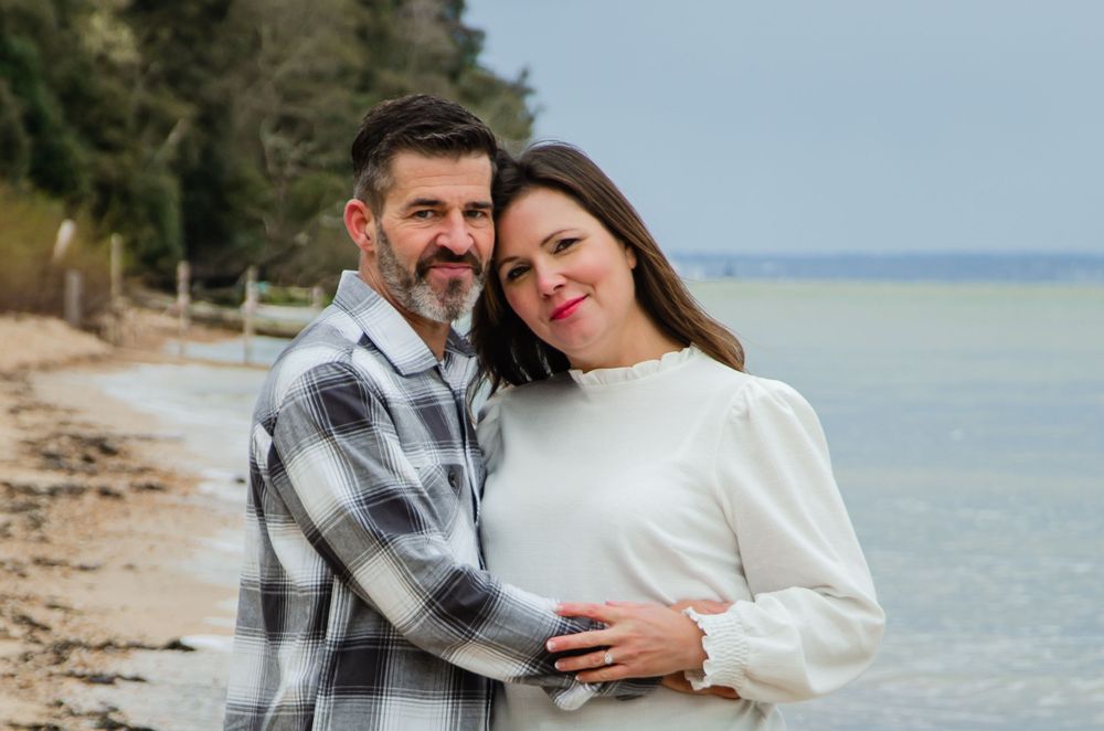 Couple embracing on beach shoreline wearing matching white and plaid outfits.