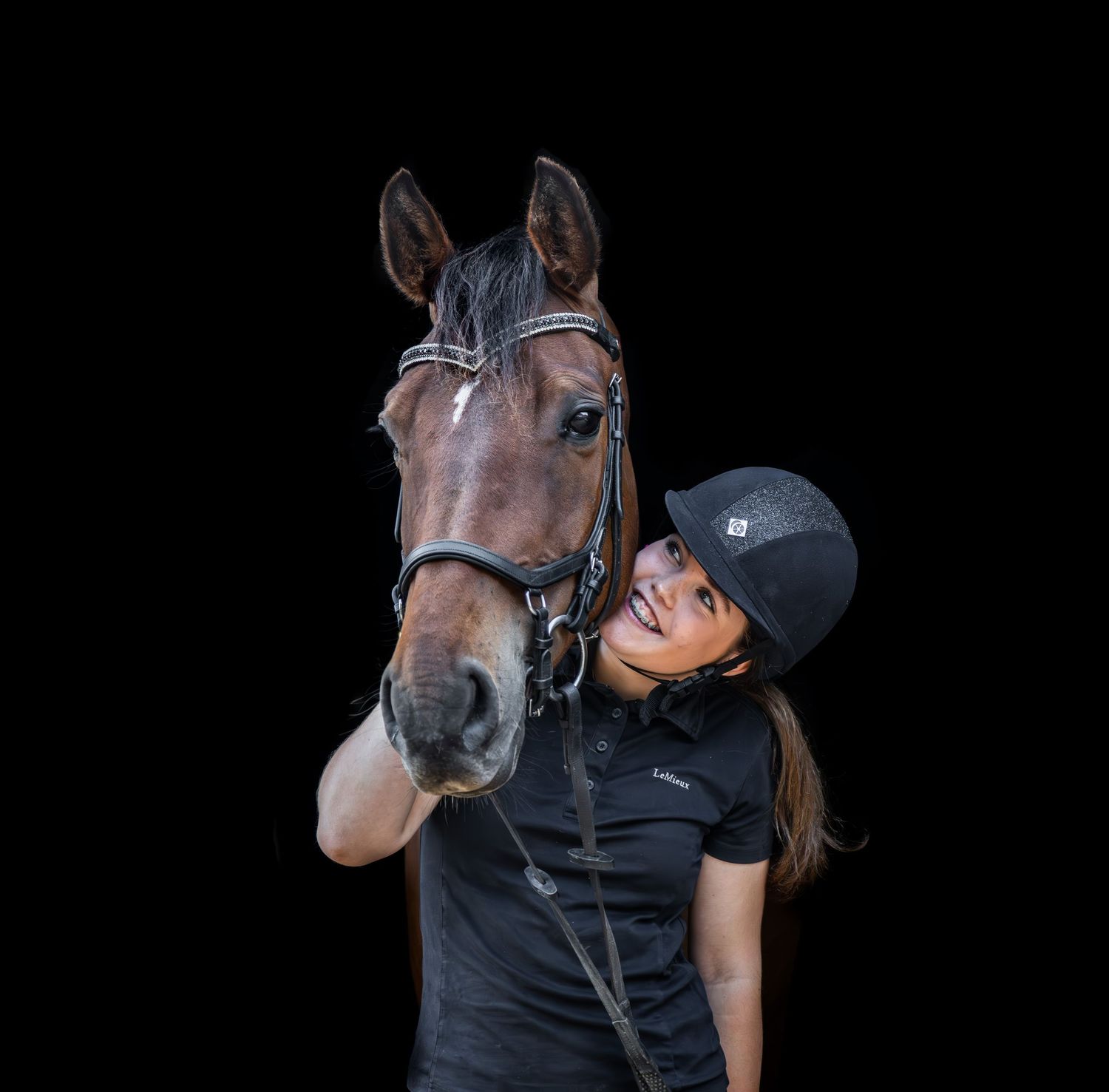 A bay horse and rider in equestrian gear pose against a black background.