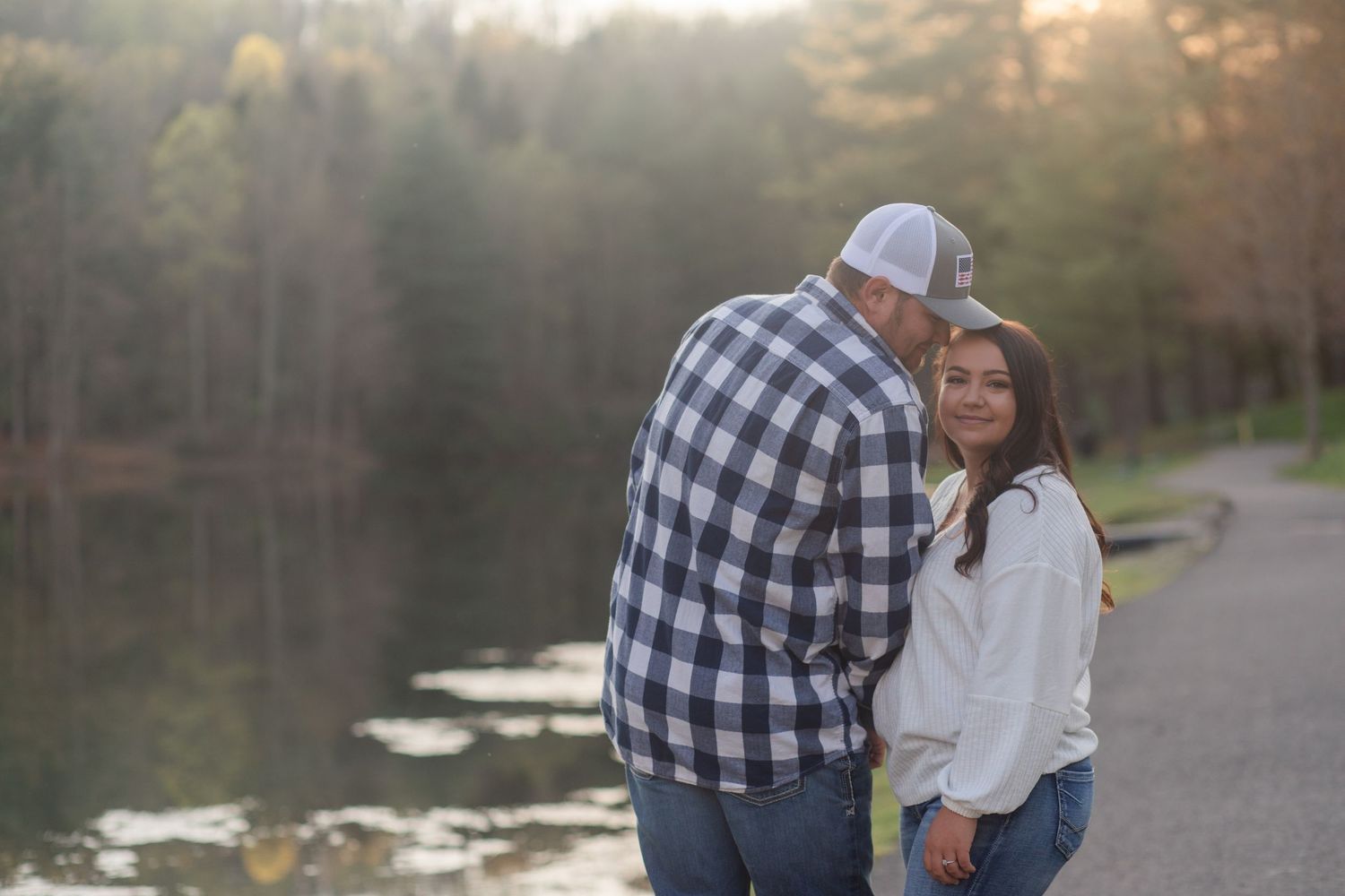 Couple in casual winter wear shares tender moment by lake during evening light.