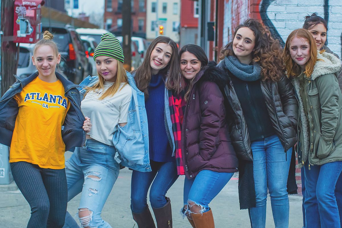 Group of friends in casual winter wear posing together on city street.