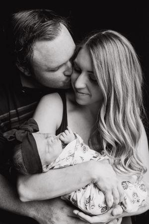 Man kisses wife on the cheek while she holds their baby girl