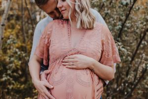Husband whisper in wife's ear as she rests hand on pregnant belly