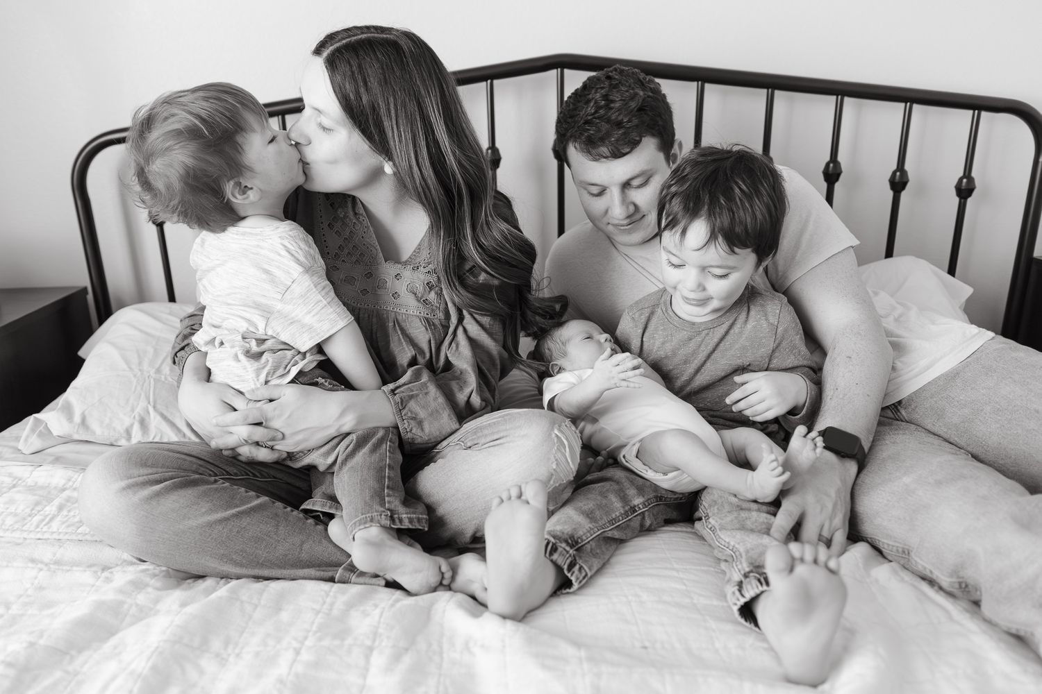 family photographer kansas city took photo of family snuggled together on master bed with husband holding baby boy and toddler