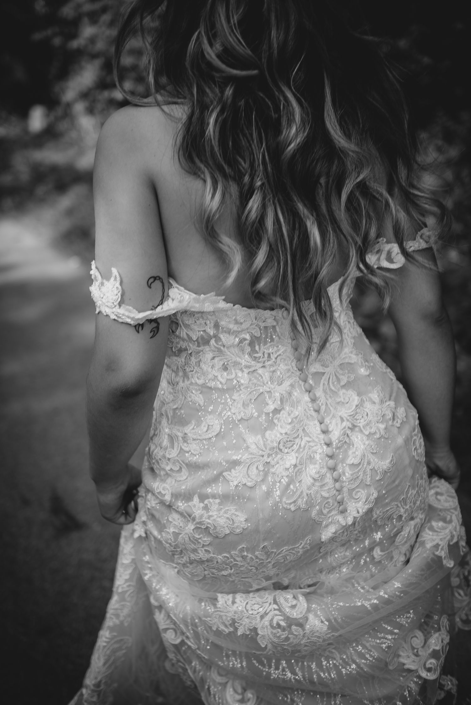 Black and white image showing back detail of an ornate lace wedding dress with cascading wavy hair.