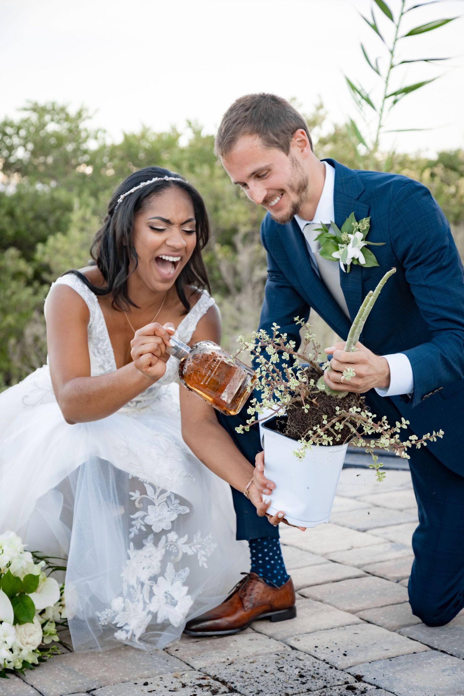 A joyful couple in wedding attire shares a candid moment outdoors with flowers and rustic decor elements.