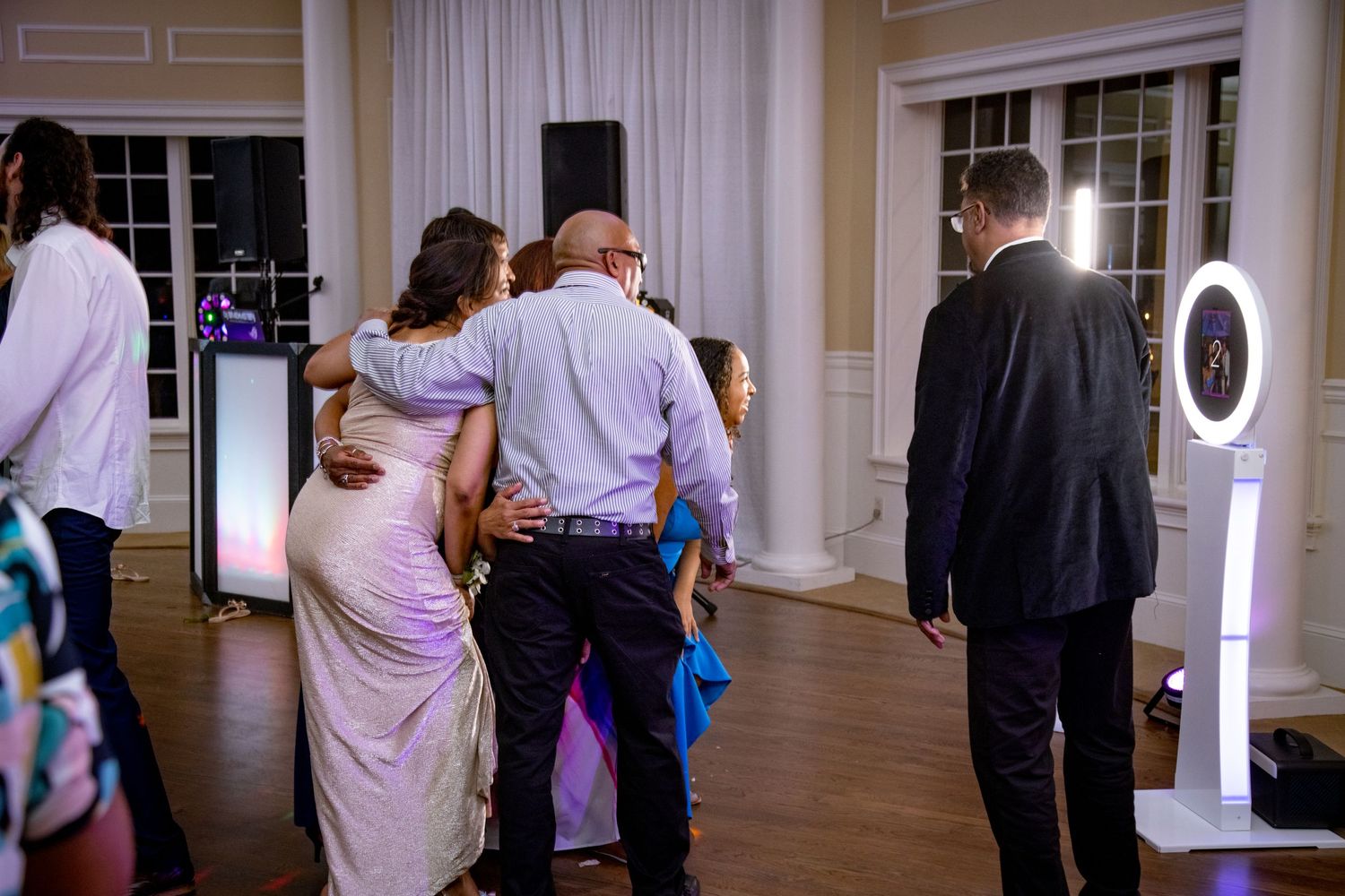 Wedding guests line up to take photos at a photo booth station with a ring light setup during an indoor reception.