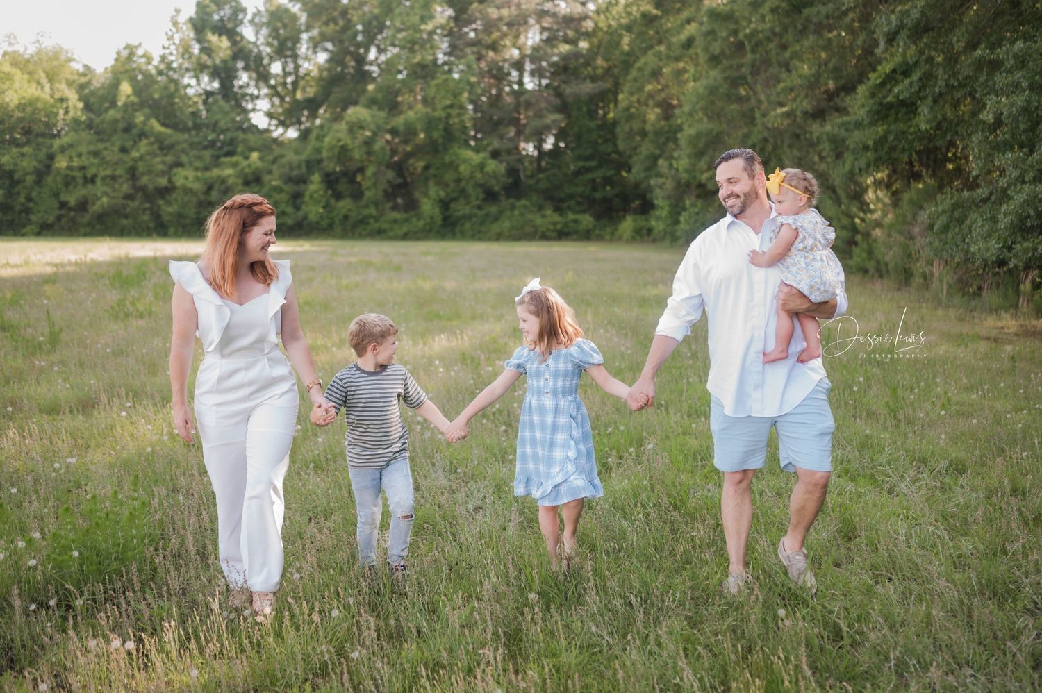 Family walking together holding hands in a sunny meadow during golden hour.