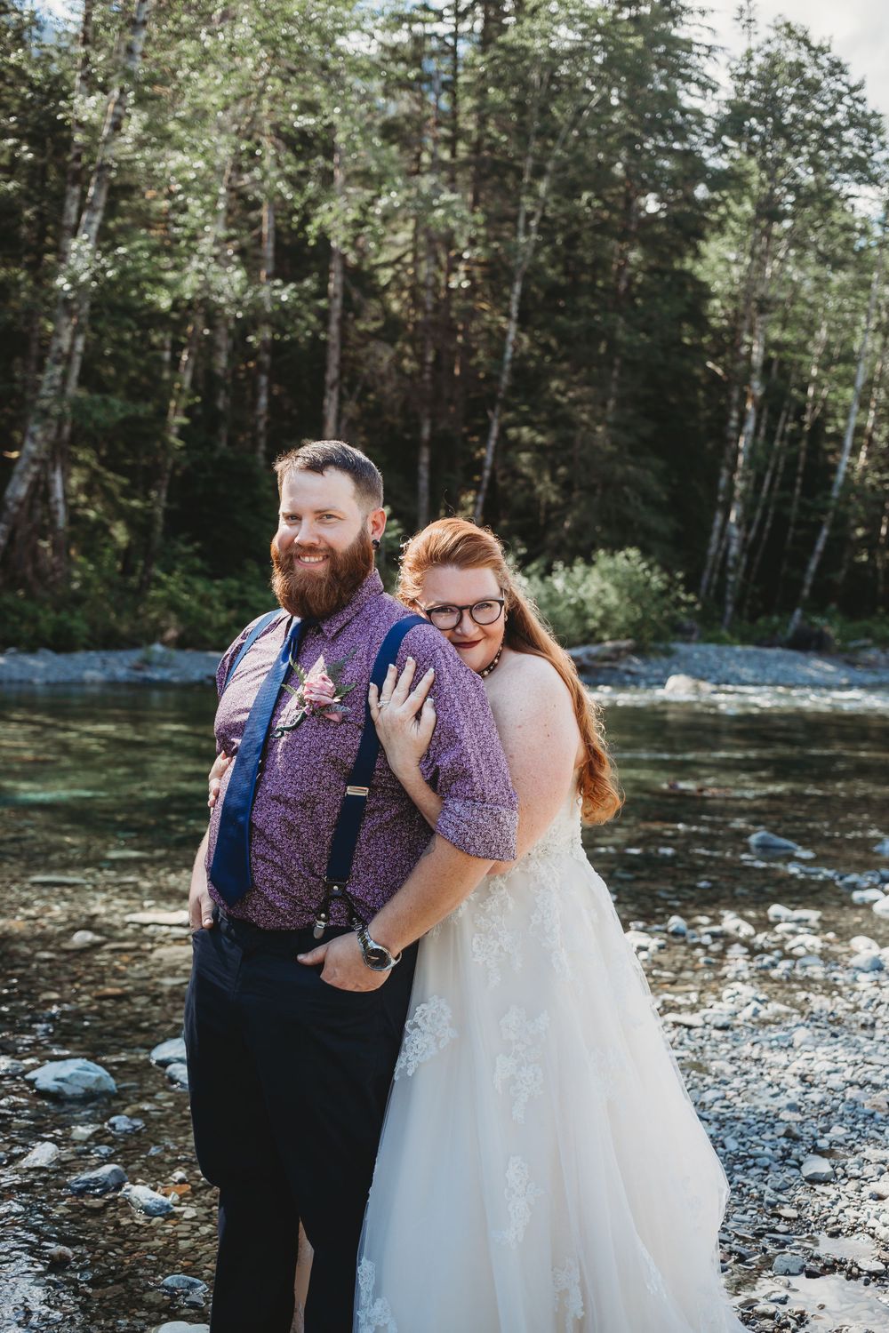 Bride hugs groom from behind along the river at their mountain elopement