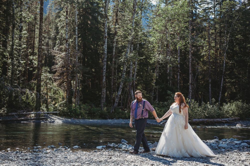 Bride and groom walk along the river hand in hand at their mountain elopement