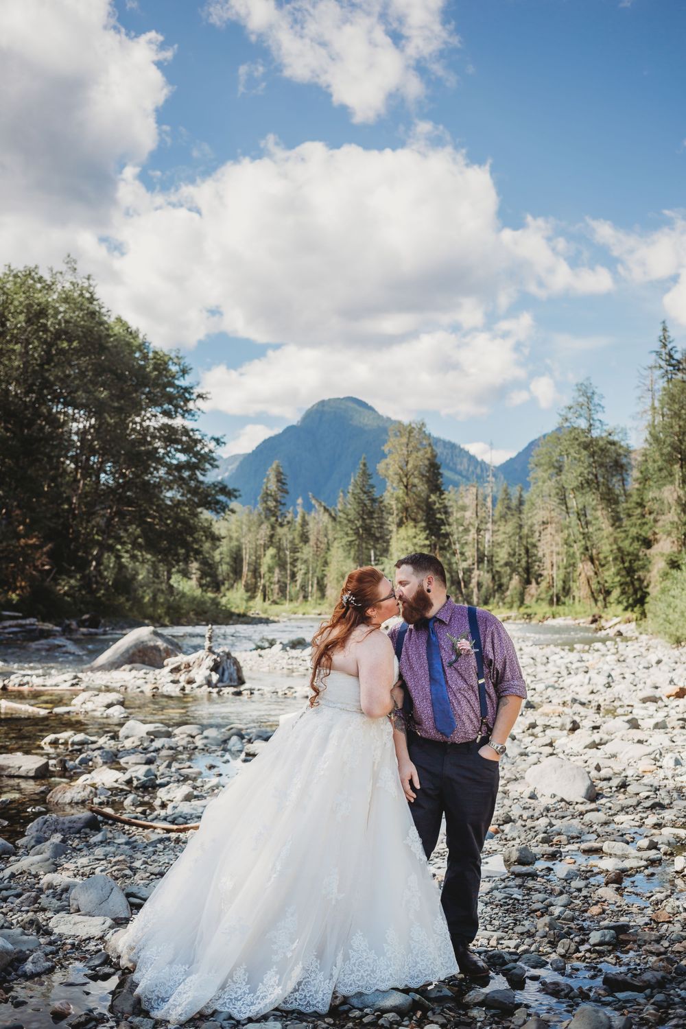 Bride and groom kiss standing in the water and rocks of a river in the mountains at their elopement