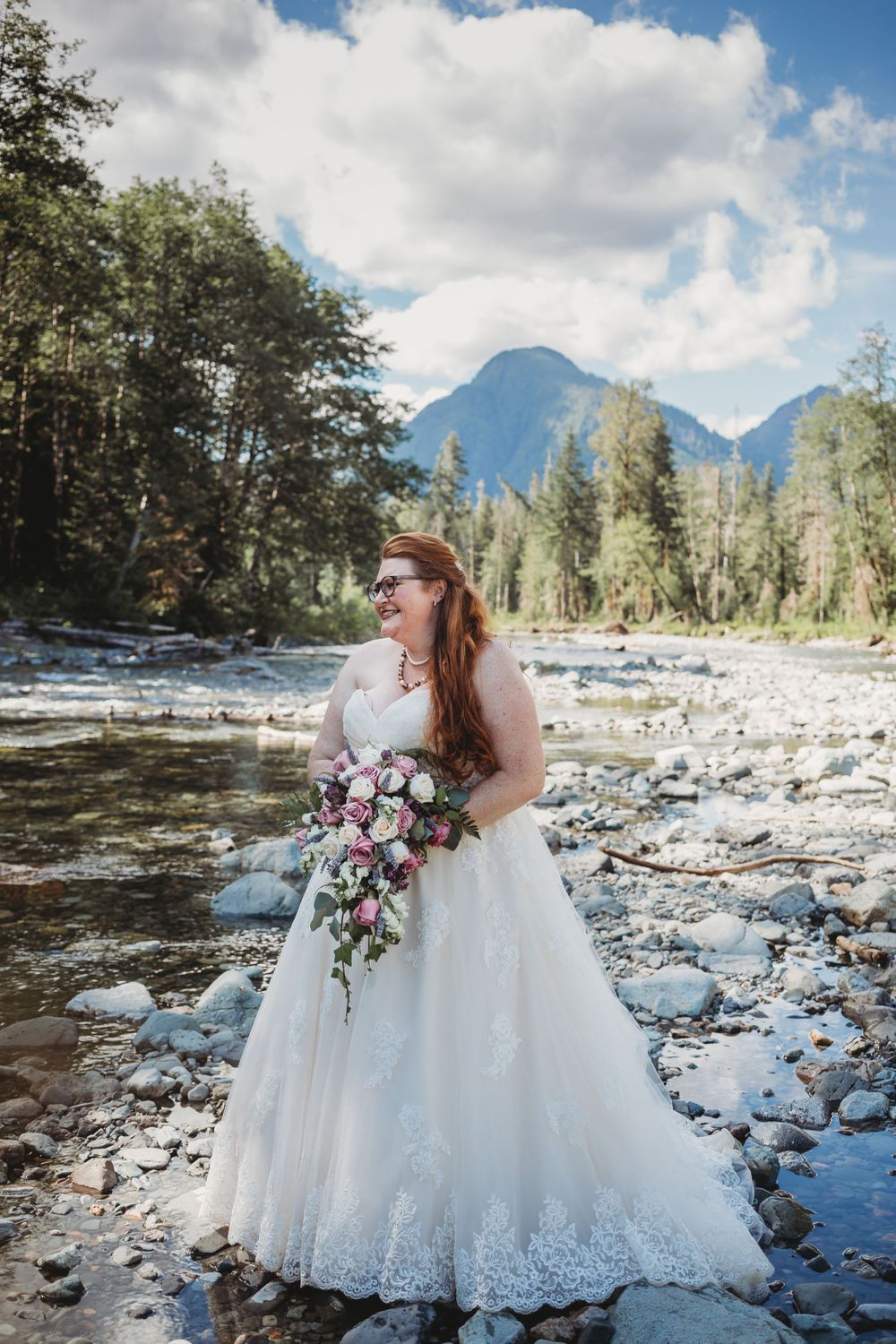 Bride holds her bouquet along the river in the mountains at her elopement